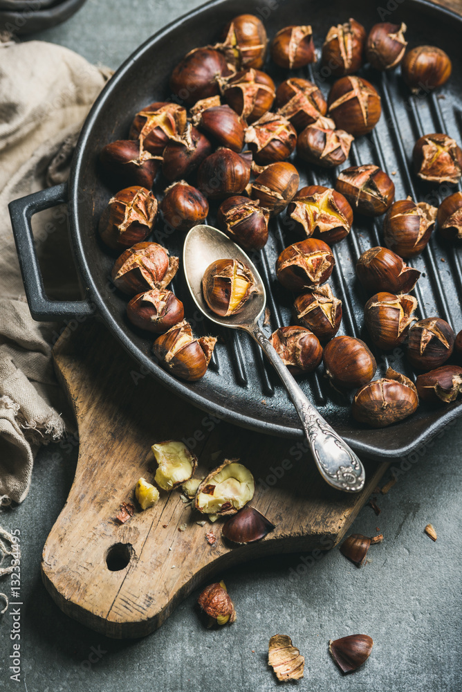 Roasted chestnuts in cast iron grilling pan over rustic wooden board and grey concrete stone backgro