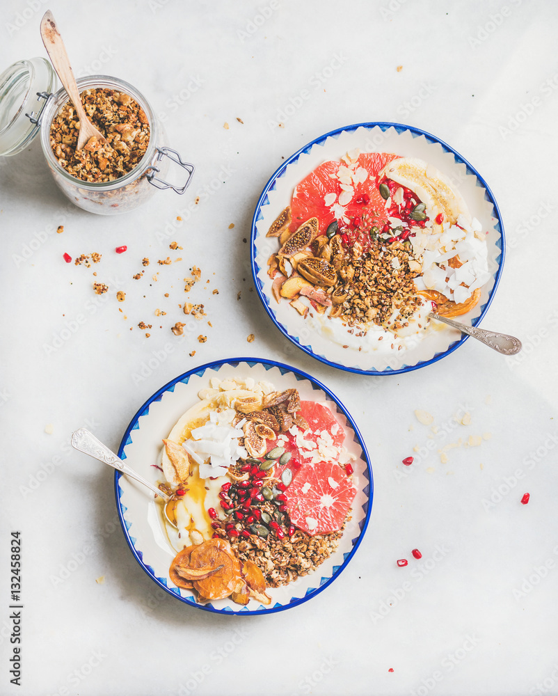 Healthy breakfast yogurt bowls with granola, grapefruit, banana, pomegranate, dried fruit, nuts, see