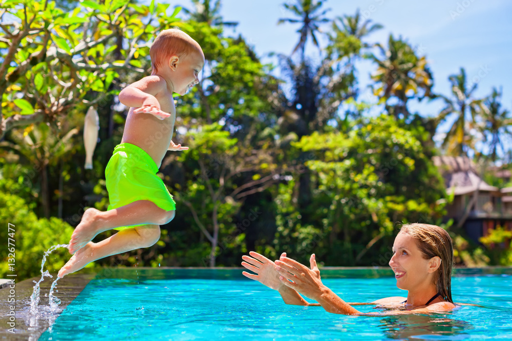 Happy child in action - active kid swim with fun in swimming pool. Baby son jump high to mother catc