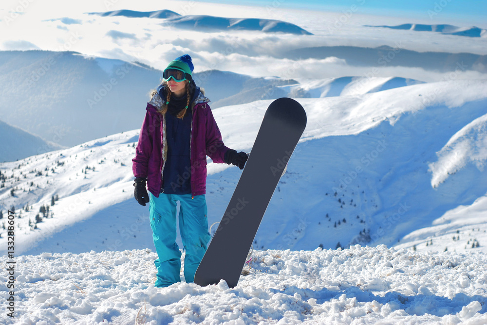 girl standing on a mountain top with snowboard in the hands