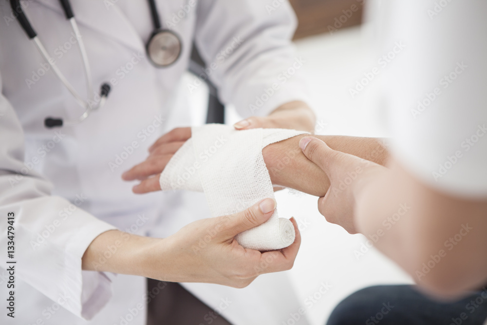 The doctor is wrapping a bandage in the hand of a man