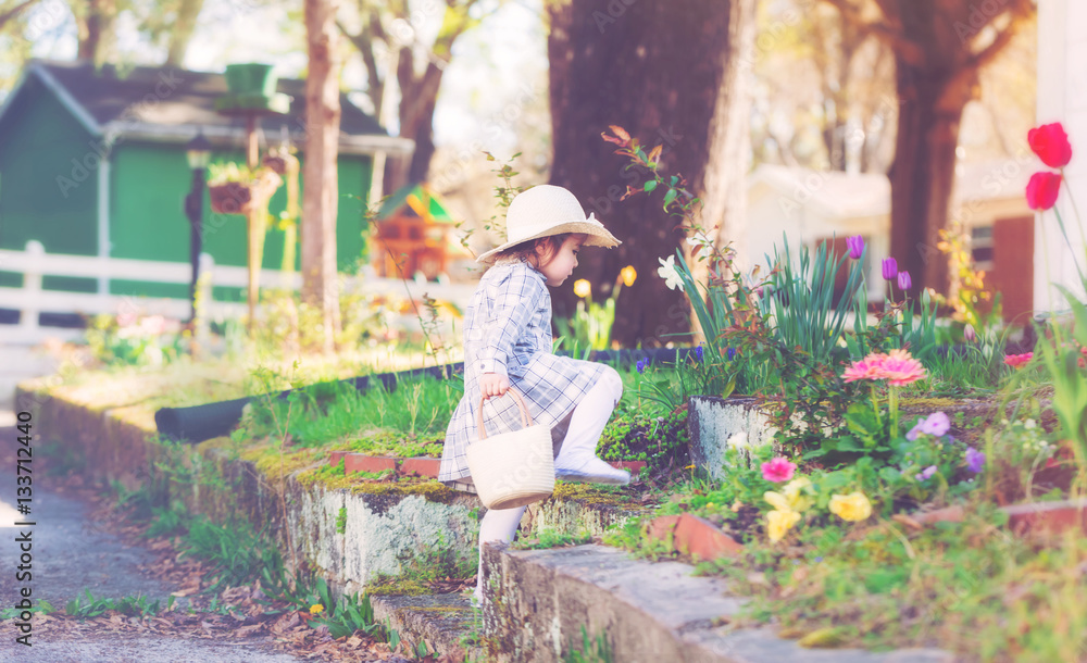Toddler girl in a hat exploring her spring garden