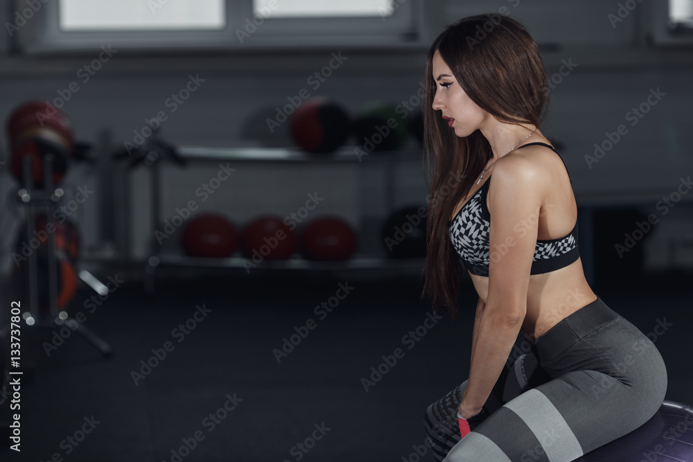 Young beautiful woman sit on fitness ball in gym.