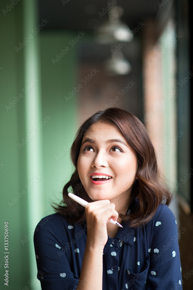 Young beautiful woman in the cafe near the window, thinking and writing something.