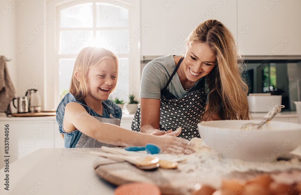 Happy young girl with her mother making dough