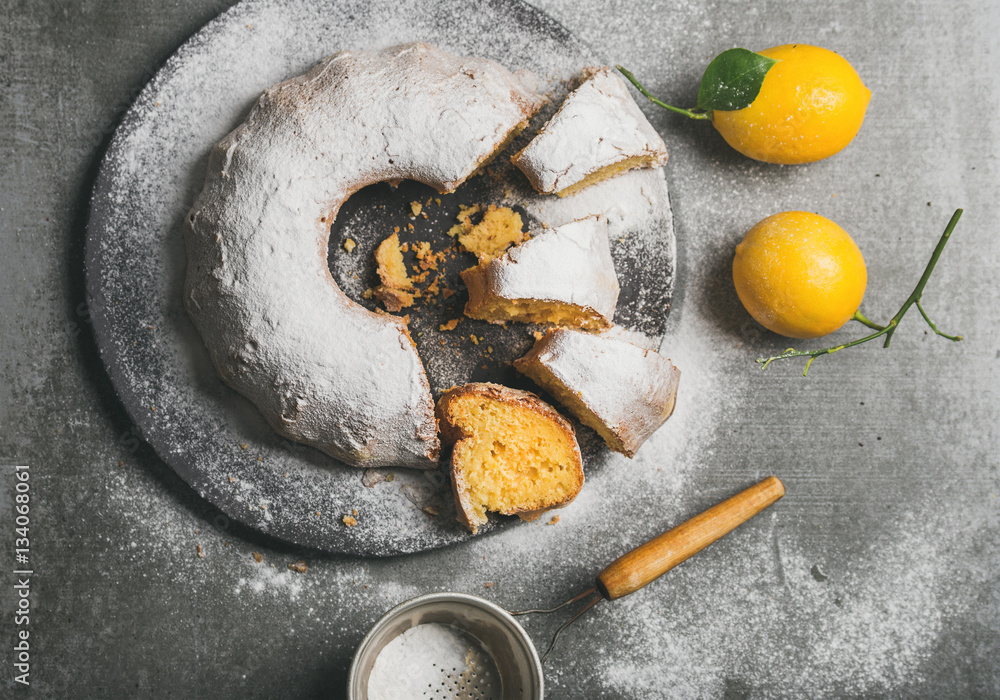 Homemade gluten-free lemon bundt cake with sugar powder served with freshly picked lemons over grey 