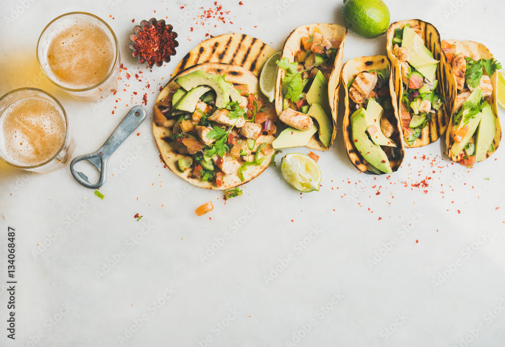 Healthy corn tortillas with grilled chicken, avocado, fresh salsa, limes and beer in glasses over li