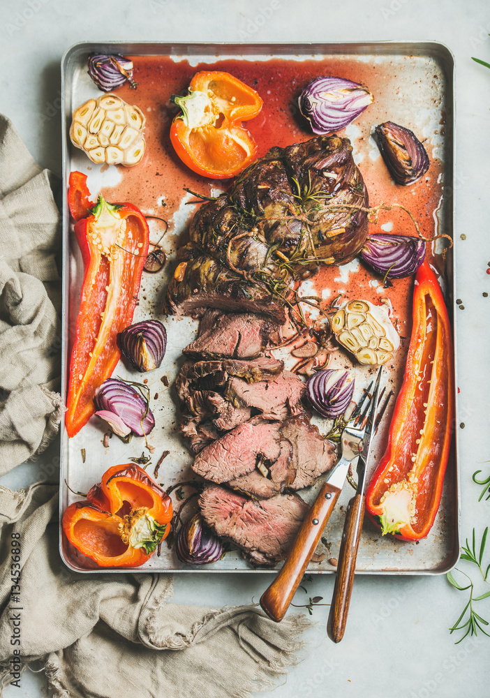Cooked Roastbeef meat with roasted vegetables and herbs in metal baking tray over grey marble backgr