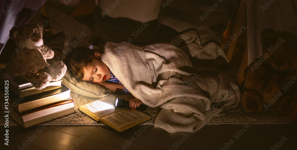 小女孩拿着书和手电筒睡在帐篷里