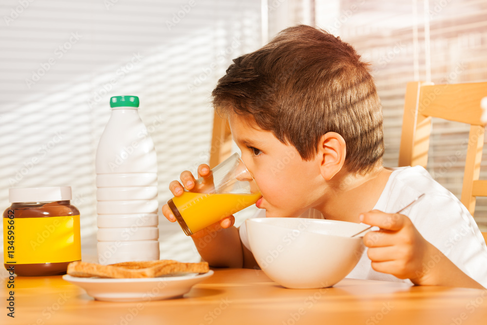 Little boy drinking orange juice at breakfast