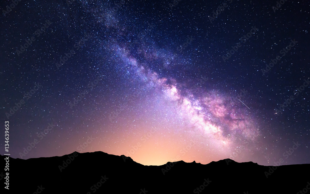 Night landscape with colorful Milky Way and yellow light at mountains. Starry sky with rocks at summ