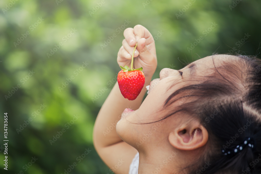 美丽的微笑小女孩在花园里吃草莓