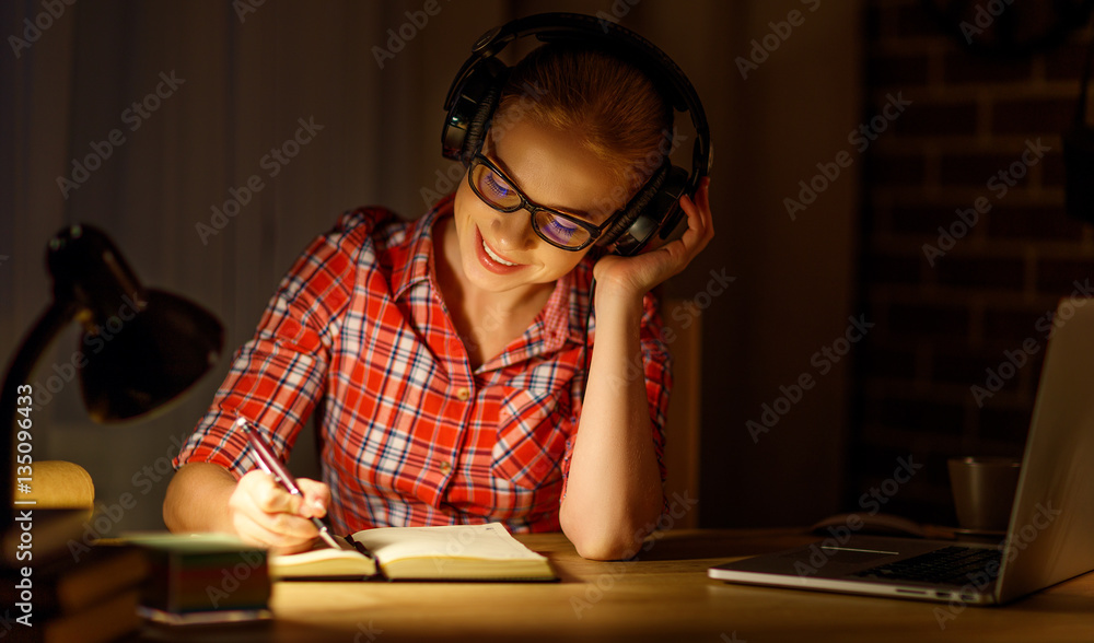 young woman student in headphones working on the computer at nig