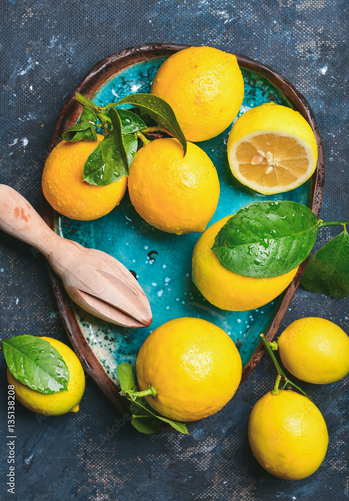 Close-up of freshly picked lemons with leaves in bright blue ceramic plate over dark blue shabby ply