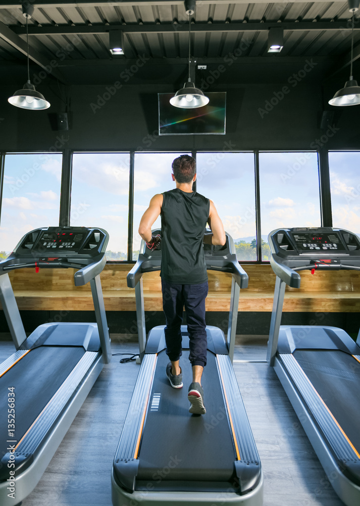 Back view of young man athlete with running on treadmill in gym.