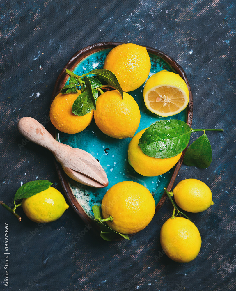 新鲜采摘的柠檬，叶子装在蓝色陶瓷盘中，背景为深蓝色破旧，俯视图。