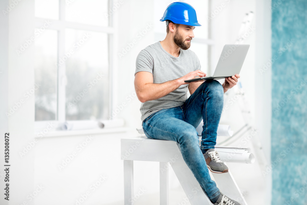 一位英俊的建筑工人、工头或修理工的肖像，戴着头盔，手里拿着白色笔记本电脑