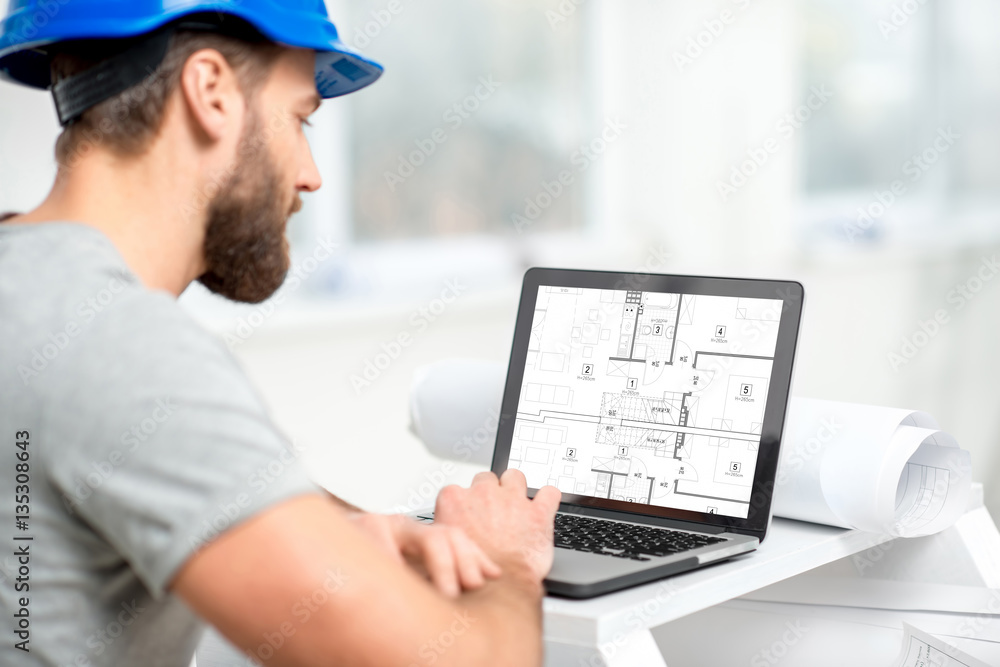 Handsome architect or foreman in helmet working with laptop on the apartment drawings at the structu