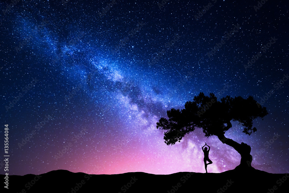银河系，有一棵老树和一个站着练习瑜伽的女人的剪影。美丽的风景