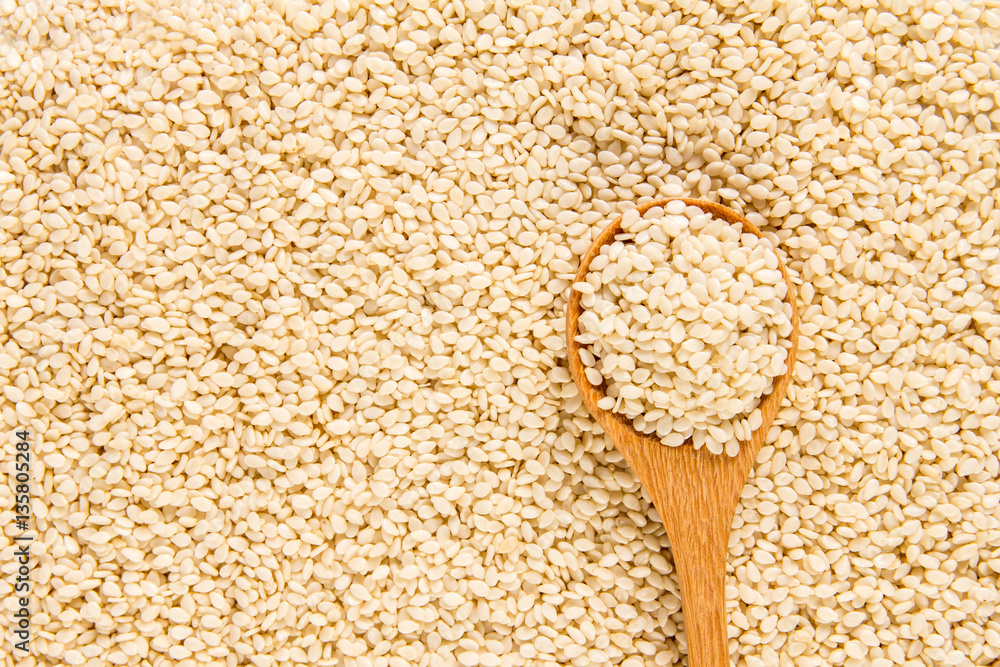close up sesame in wooden spoon on white sesame seeds surface 
