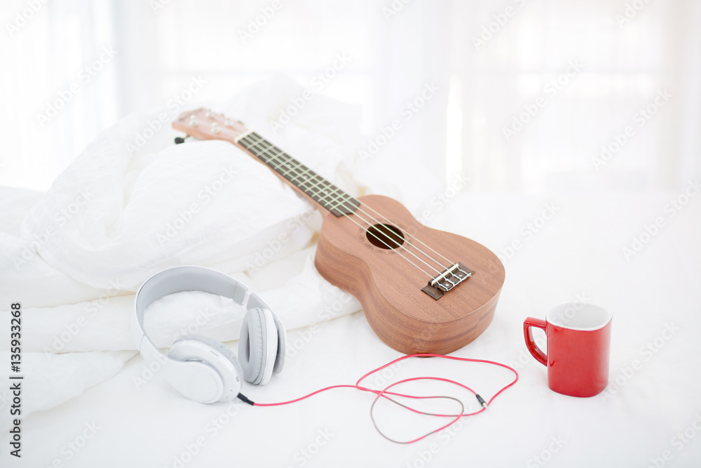 Classic Ukulele guitar on bed with headphone and coffee cup