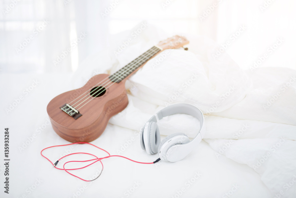 Classic Ukulele guitar on bed with headphone