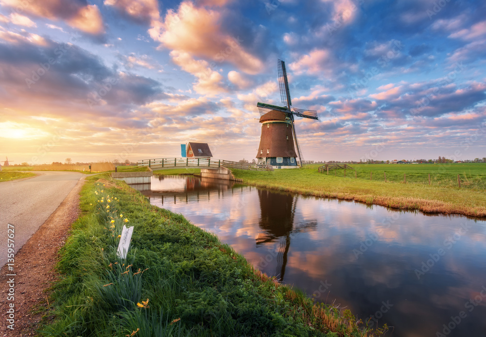 Windmill near the water canal at sunrise in Netherlands. Beautiful old dutch windmill against colorf