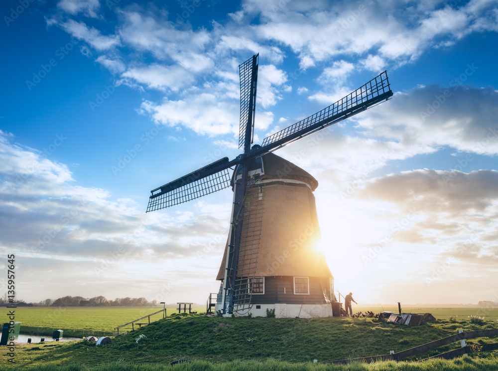 Windmill and silhouette of a man at sunrise in Netherlands. Beautiful old dutch windmill against col
