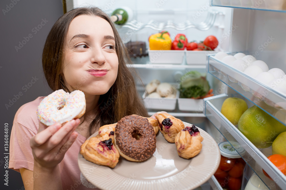 穿着睡衣的年轻女子在冰箱附近吃甜甜圈