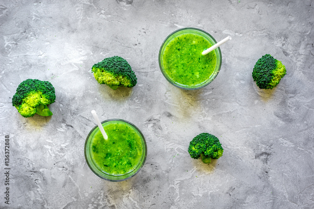 Green vegetable smoothie in glass at gray background top view