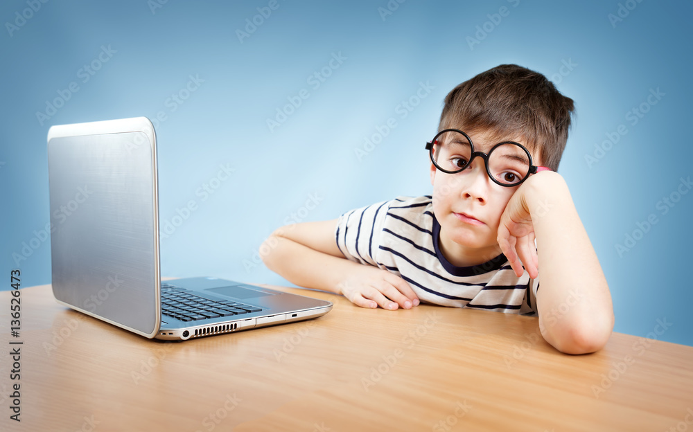 seven years old child in glasses sitting with a laptop at table