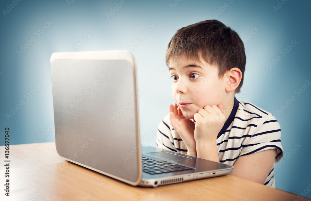 surprised seven years old child sitting with a laptop at table