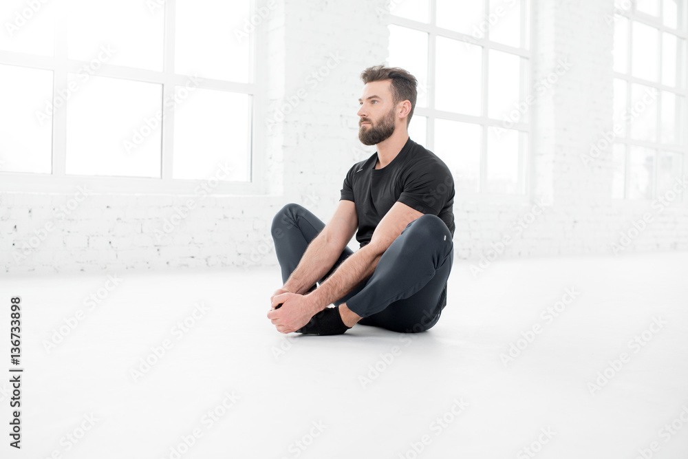 Handsome man in the black sportswear doing yoga in the white gym interior