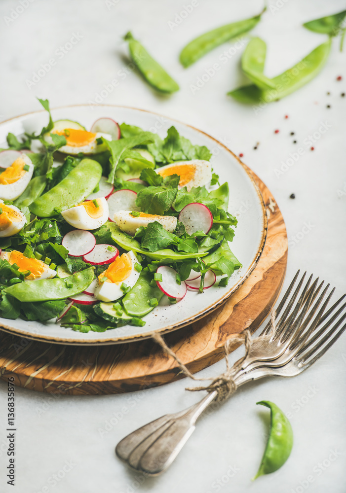 Healthy spring green salad with radish, boiled egg, arugula, green pea and mint in white plate on ol