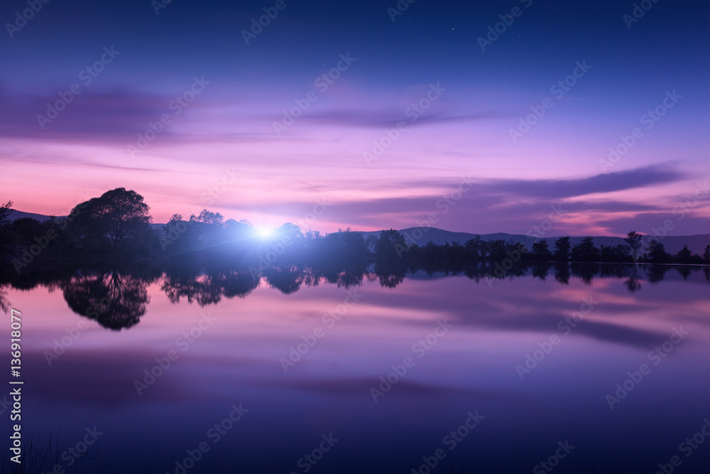 Mountain lake with moonrise at night. Night landscape with river, trees, hills, moon and colorful pu