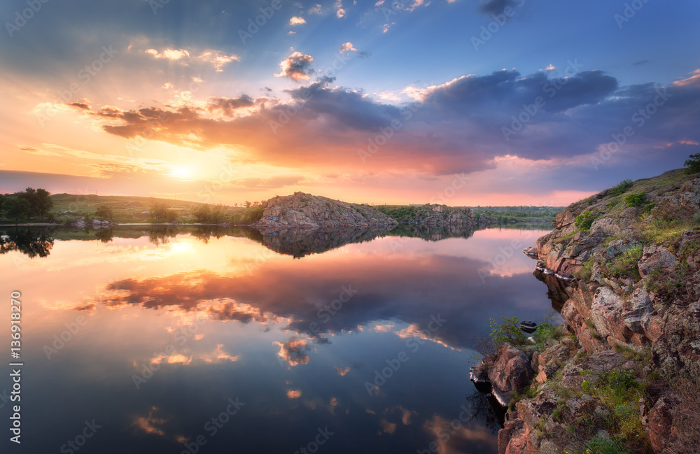Lake against colorful sky with clouds and rocks at sunset in summer. Beautiful landscape with river,