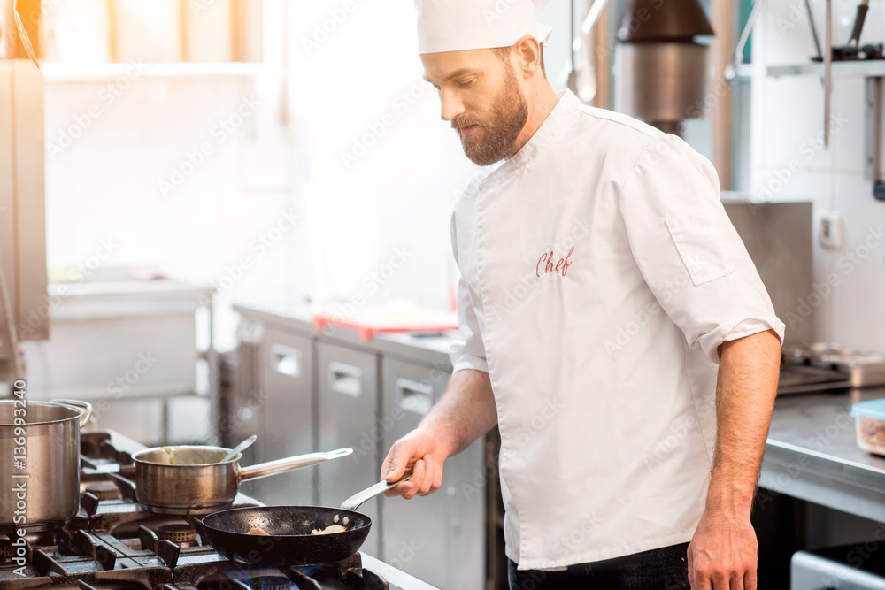 Handsome chef cook in uniform cooking food on the gas stove at the restaurant kitchen