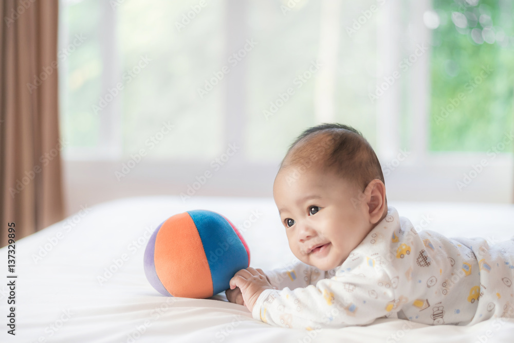 4个月大的亚洲婴儿躺在家里卧室的白色床上玩彩色球的肖像。