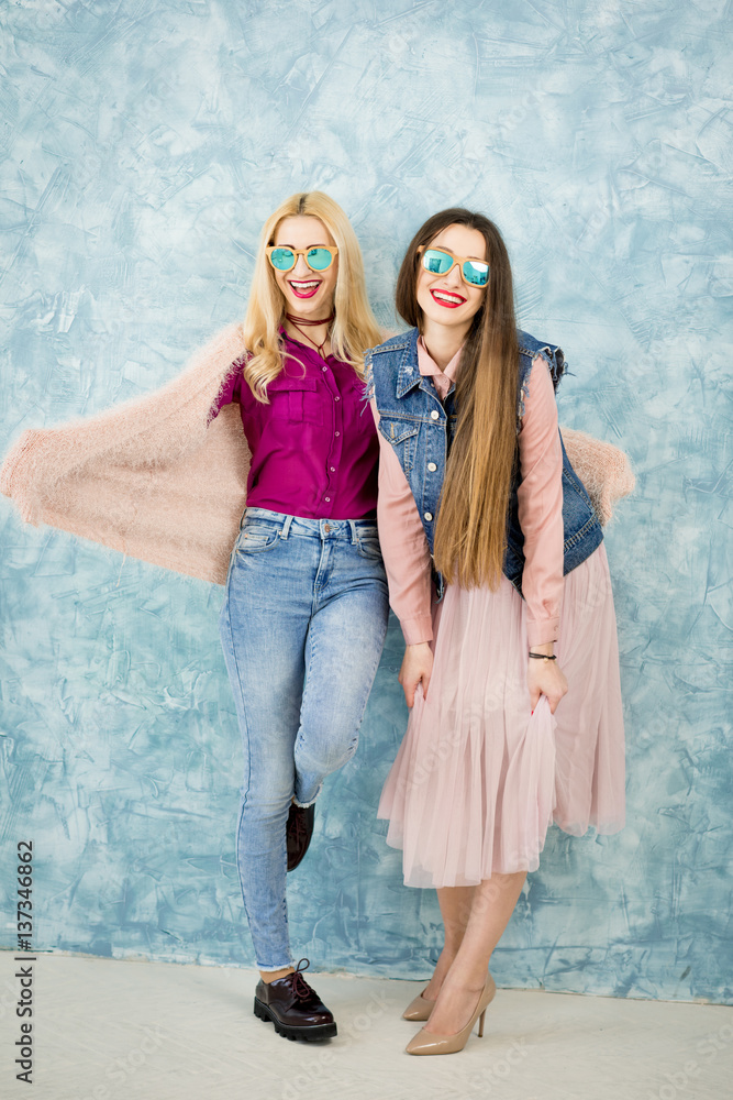 Female stylish friends having fun together on the blue wall background