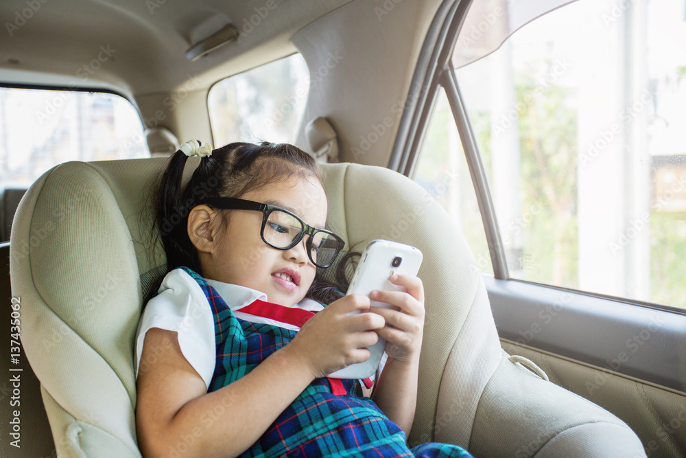 可爱的小女孩躺在儿童汽车座椅上玩智能手机