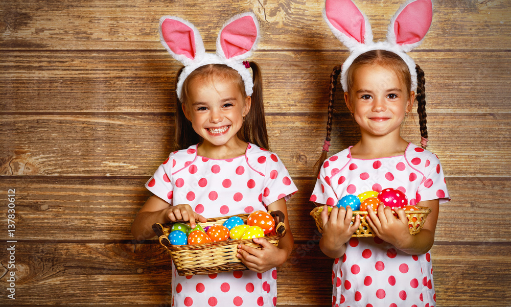 复活节快乐！可爱的双胞胎女孩姐妹打扮成木头背景上有鸡蛋的兔子