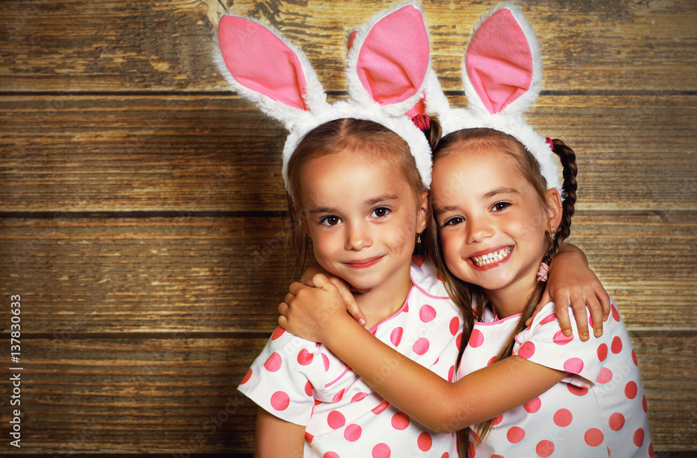 复活节快乐！可爱的双胞胎女孩姐妹打扮成木头背景的兔子