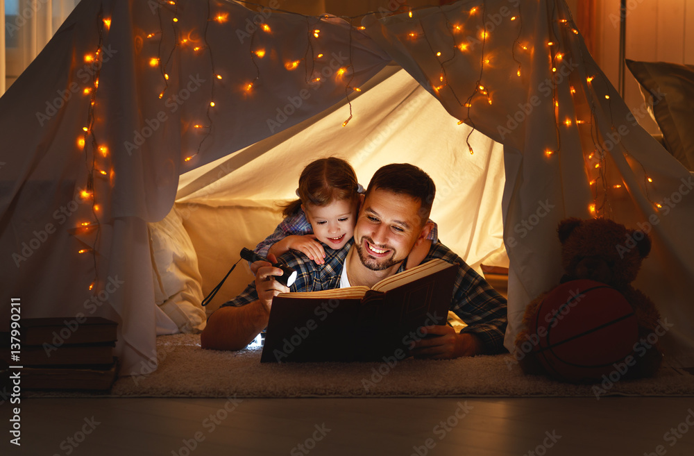 happy family father and child daughter reading a book  in  tent at home.