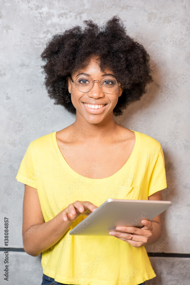 Portrait of a beautiful african woman in yellow t-shirt with digital tablet near the gray wall indoo