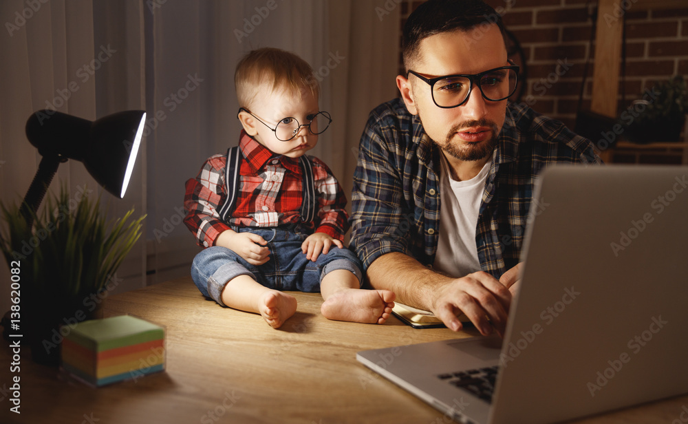父亲和儿子婴儿在黑暗中在家里用电脑工作