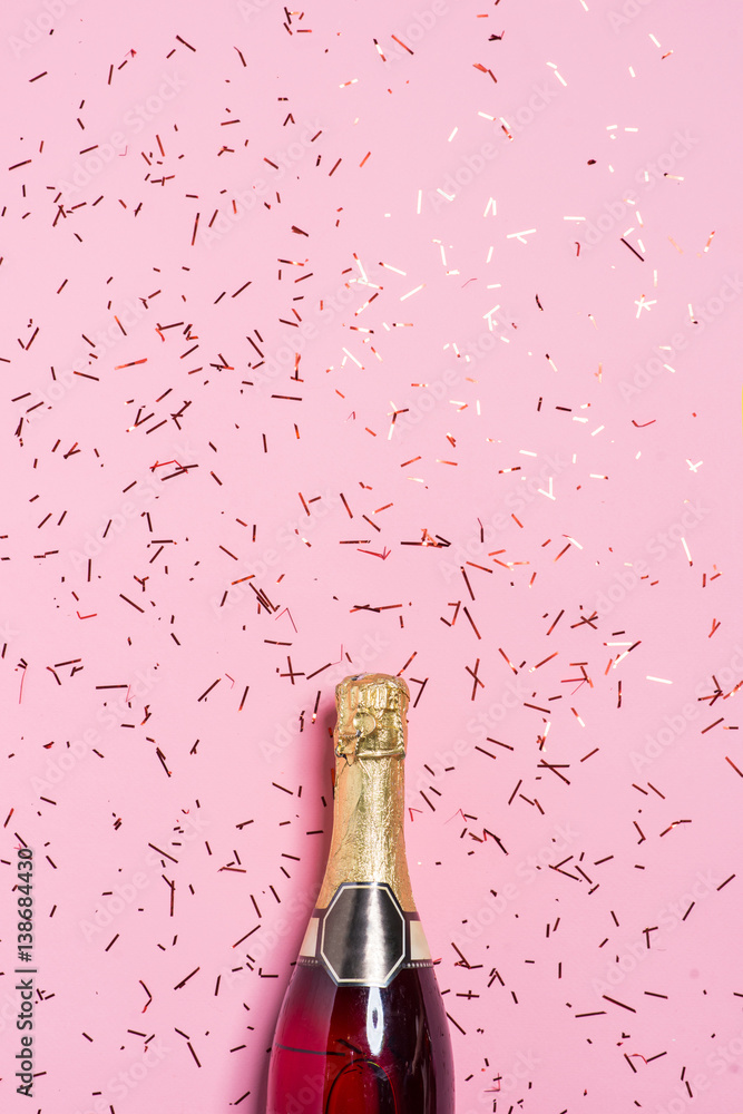 Flat lay of Celebration. Champagne bottle with colorful party streamers on pink background.