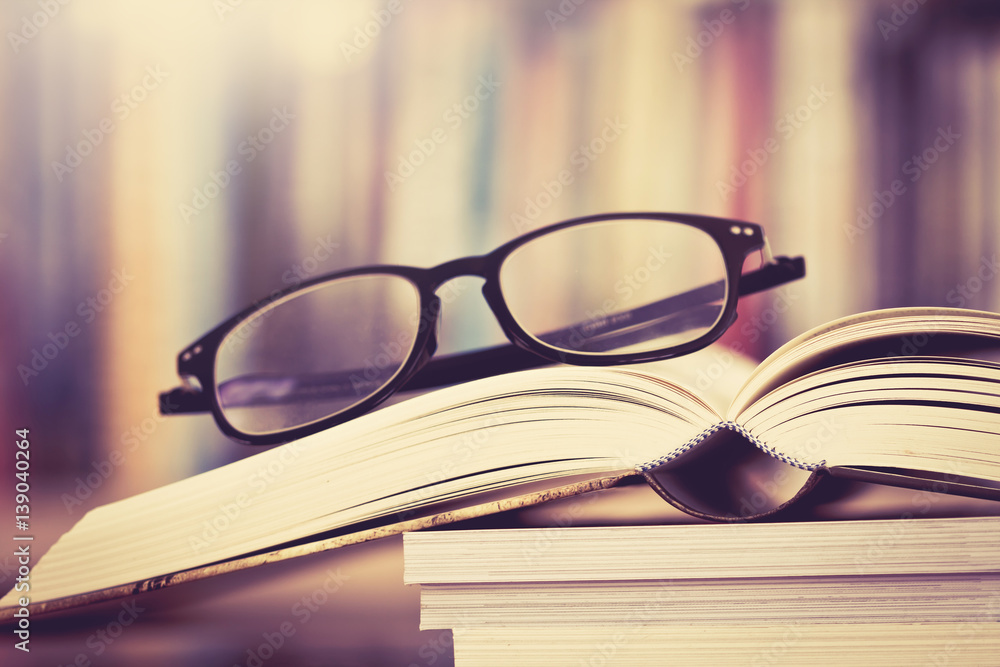 Close up opened book page and  reading eyeglasses with  blurry bookshelf background for education an