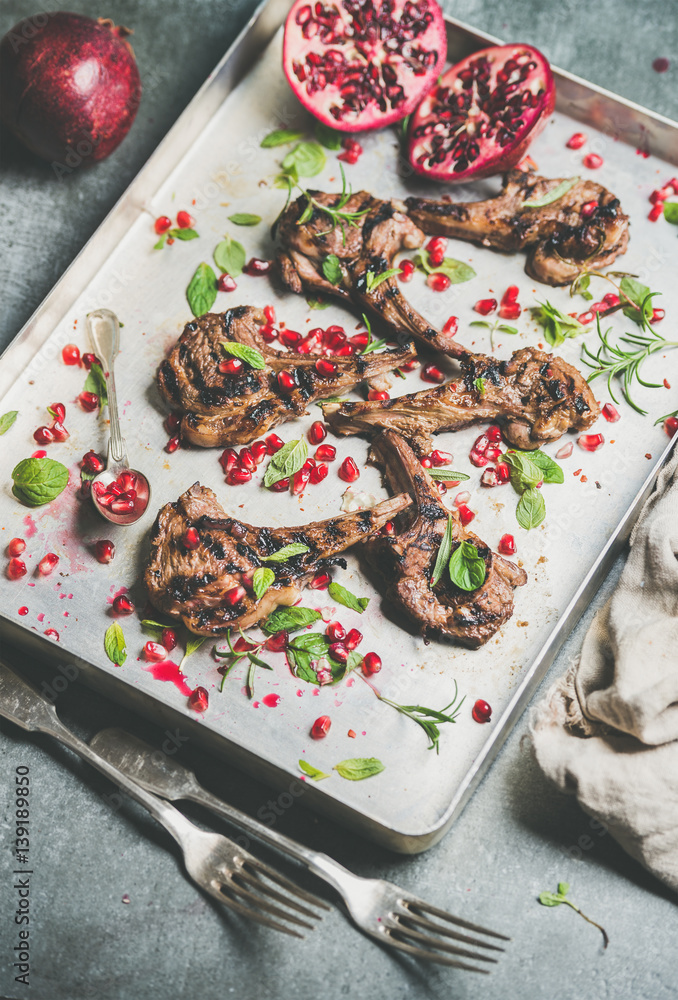Grilled lamb ribs with pomegranate seeds, fresh mint and rosemary in metal baking tray over grey con