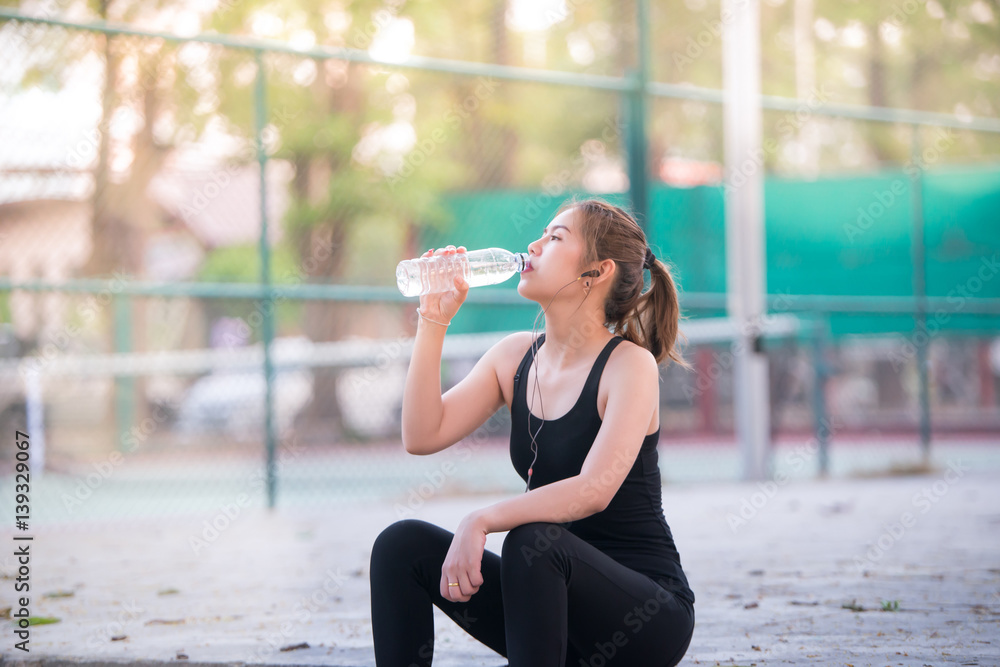 Asian young Fitness woman drinking water after jogging with Tennis court background