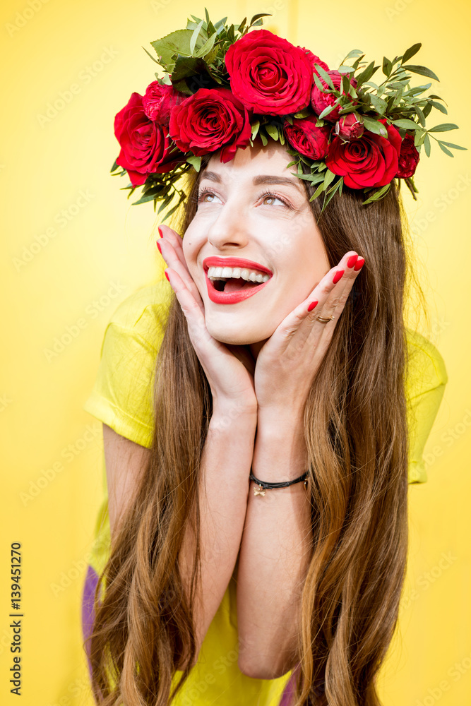 Colorful portrait of a beautiful woman in yellow t-shirt with wreath made of red roses on the yellow